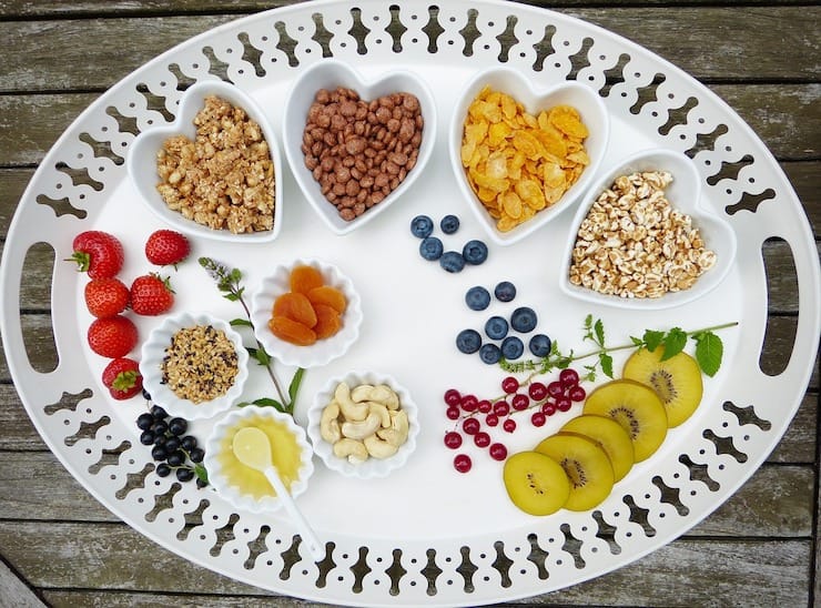 White tray with heart shaped bowls filled with cereals, fruits and nuts