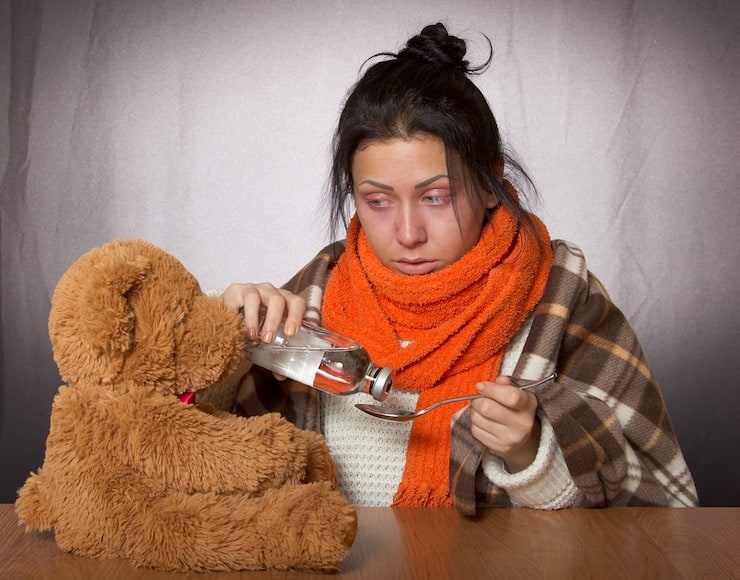 Sick woman with messy hair and oragne scarf pouring medicine onto a spoon