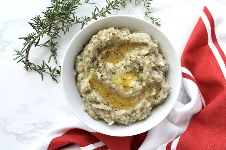 A bowl of cauliflower puree with a sprig of rosemary.