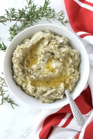 A bowl of cauliflower puree with a spoon and sprigs of rosemary.