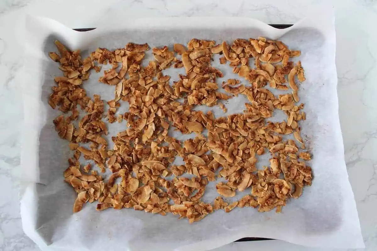 Golden brown toasted coconut flakes sprinkled with cinnamon on a parchment paper lined cookie sheet
