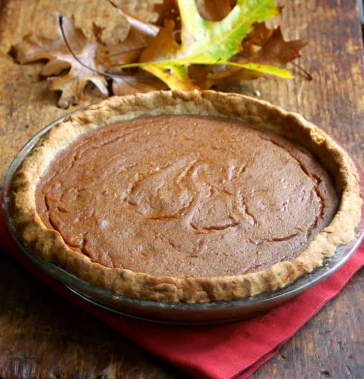 A whole pumpkin pie in a pie pan sitting on a wooden surface