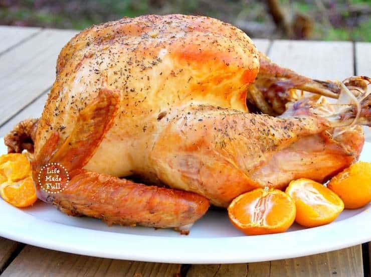 Roasted whole turkey on a white platter with mandarin oranges next to it