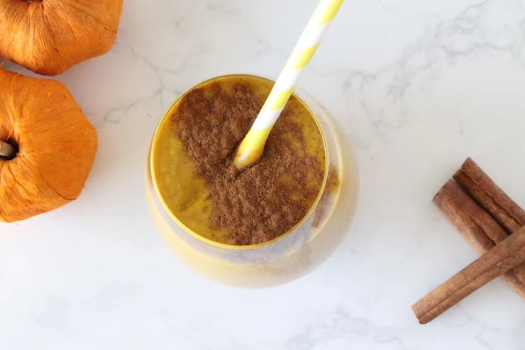 Close up of glass with orange pumpkin smoothie inside with cinnamon sprinkled on top and yellow and white striped straw inside