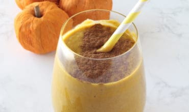 Close up of glass with orange pumpkin smoothie inside with cinnamon sprinkled on top and yellow and white striped straw inside
