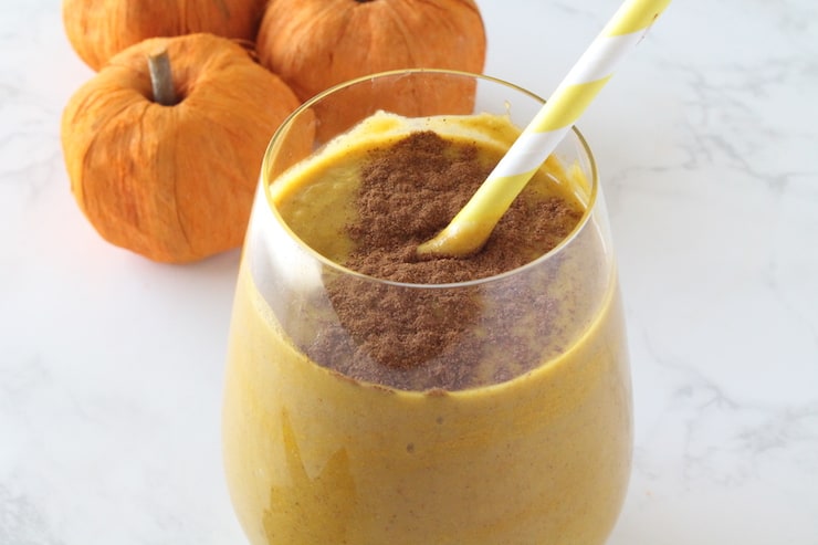 Close up of glass with orange pumpkin smoothie inside with cinnamon sprinkled on top and yellow and white striped straw inside