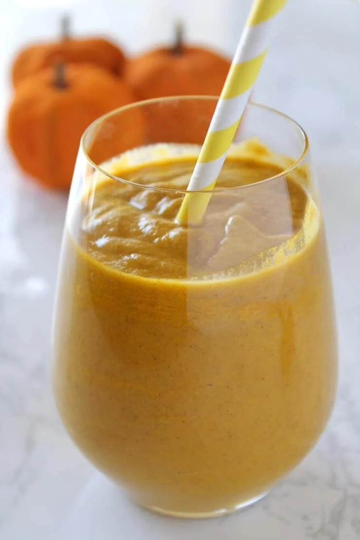 Close up of glass with orange pumpkin smoothie inside with yellow and white striped straw inside