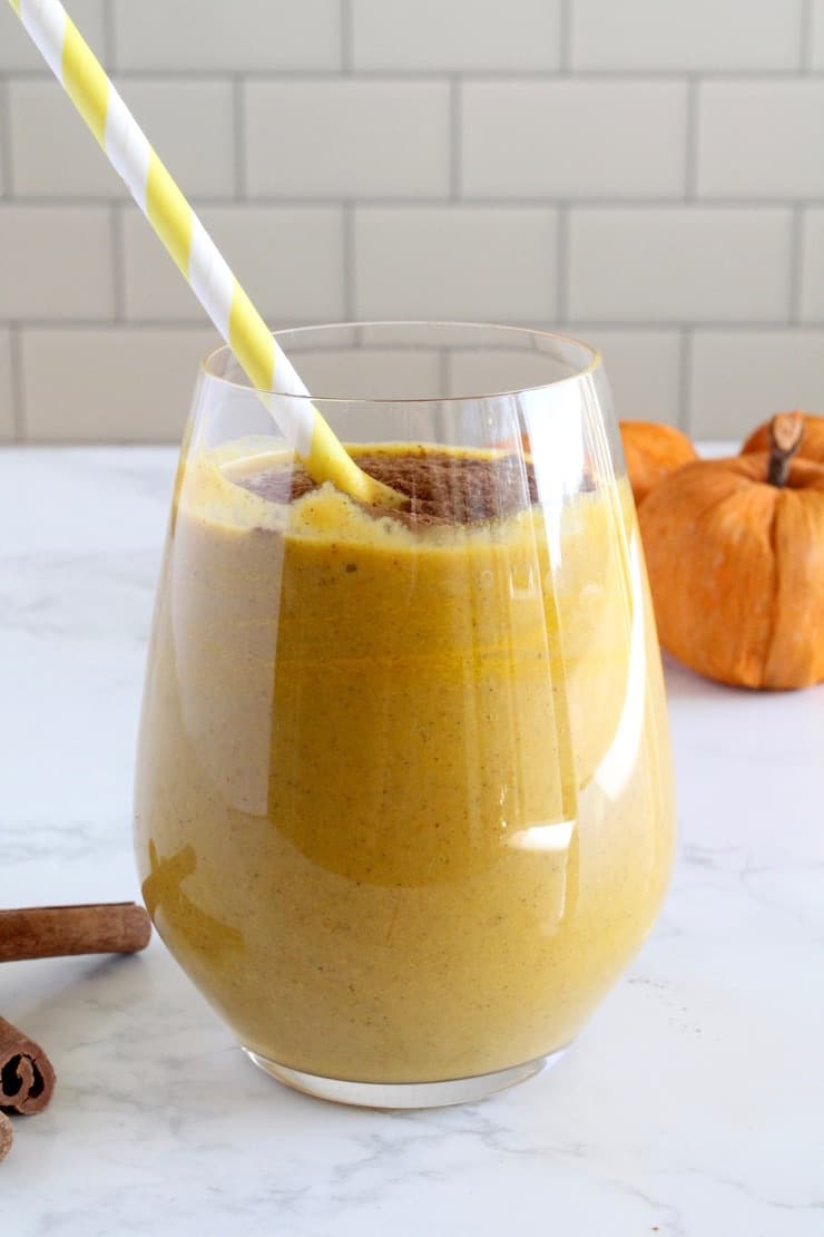 Glass with orange pumpkin smoothie inside with yellow and white striped straw inside
