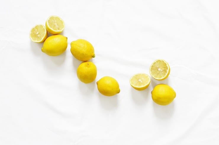 Several yellow lemons some sliced and some whole scattered on a white surface