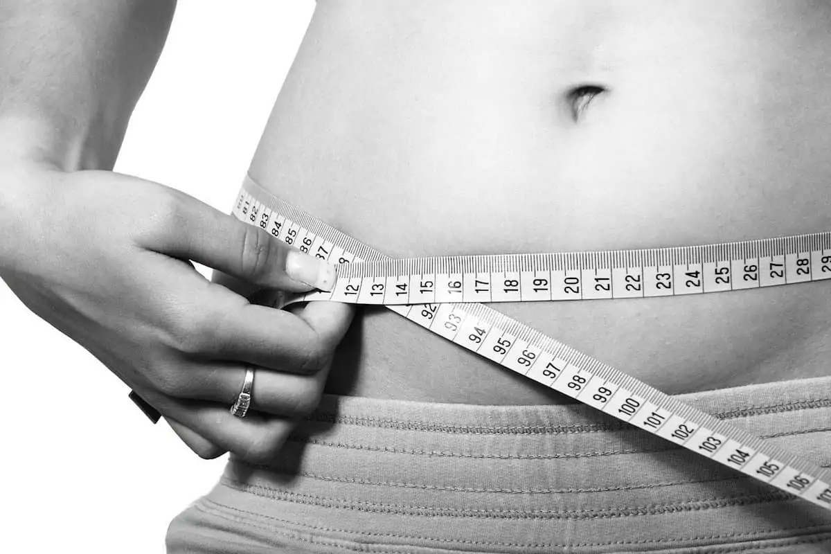 Close up on woman's abdomen with her holding a tape measure around it