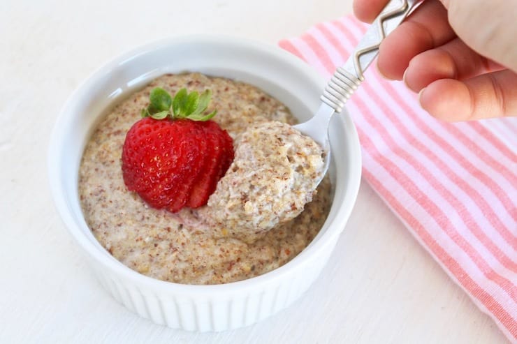 Spoon in bowl of no oats oatmeal in white bowl with strawberry on top next to pink striped towel