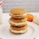three paleo pumpkin whoopie pies stacked on top of each other on a white plate with pumpkins next to it