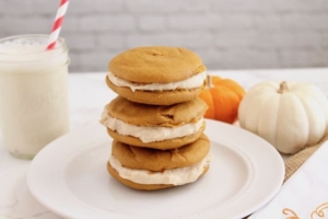 three paleo pumpkin whoopie pies stacked on top of each other on a white plate with pumpkins next to it