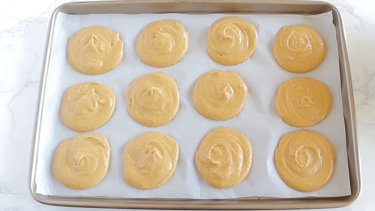 twelve heaps of uncooked cookie batter on a baking sheet lined with white parchment paper