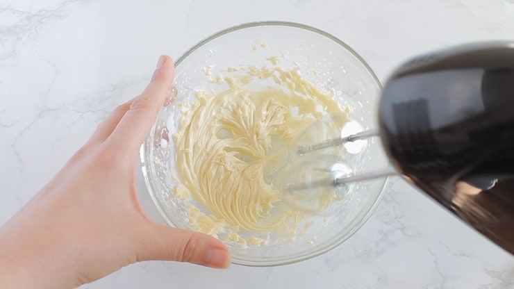 White cream filling in a clear bowl with an electric beater mixing it