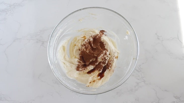 White cream filling in a clear plastic bowl with brown cinnamon added on top