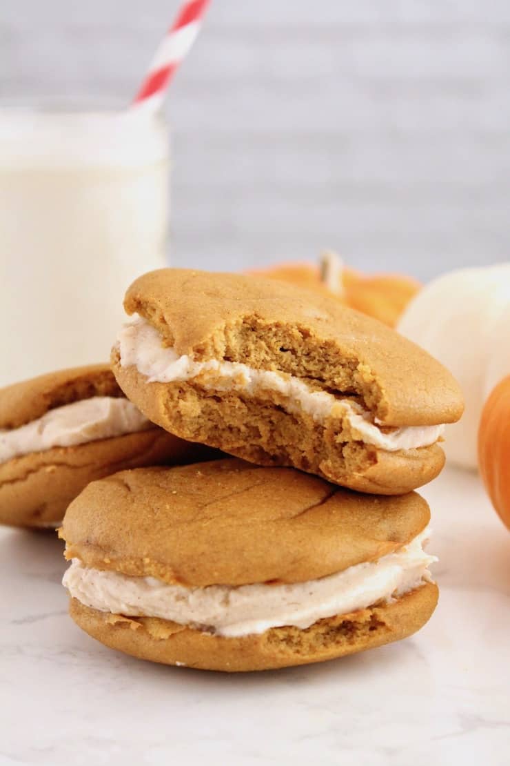 two paleo pumpkin whoopie pies on a white plate with one pie on top with a bite out of it