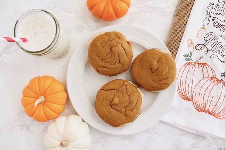 three paleo pumpkin whoopie pies lying flat on a white plate with pumpkins next to it