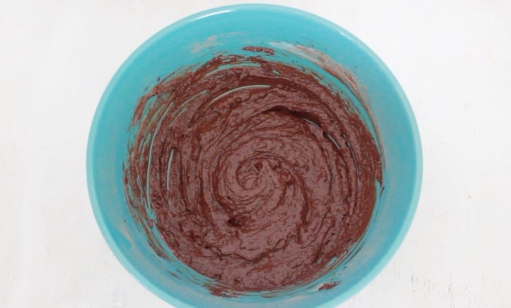 Overhead view of blue mixing bowl with brownie batter in it on white table