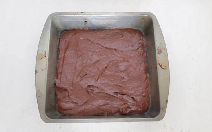 Metal pan with uncooked brownie batter in it on white table