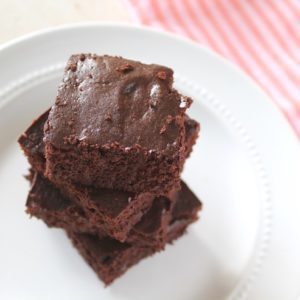 Overhead view of stacked flourless brownies on a white plate next to a pink striped dish towel