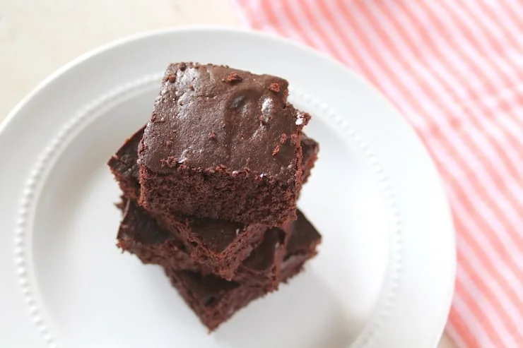 Overhead view of stacked flourless brownies on a white plate next to a pink striped dish towel