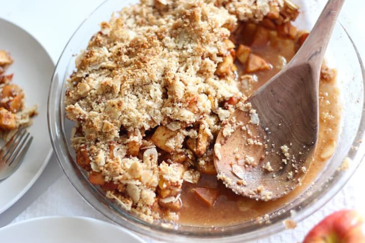 A paleo apple crisp in a glass dish with a serving spoon