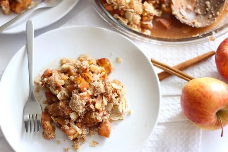 A white plate with paleo apple crisp and whole apples at the side
