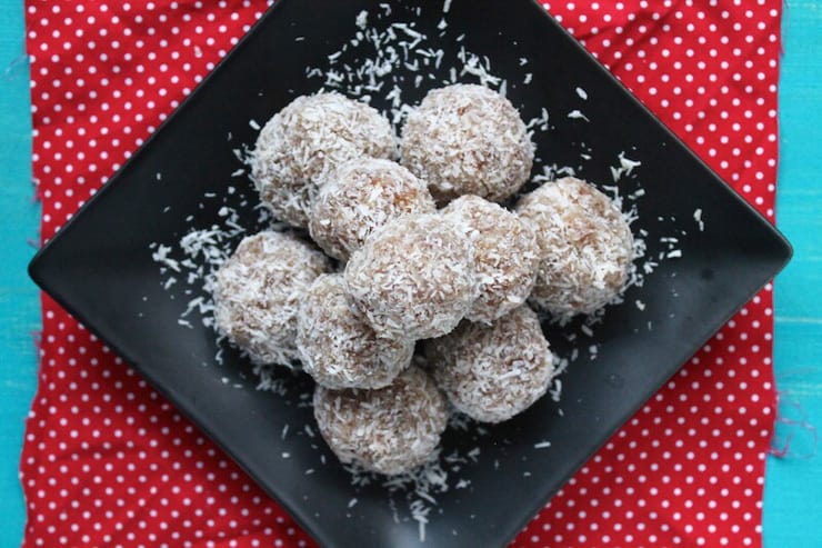 Coconut date balls in a pile on a black plate