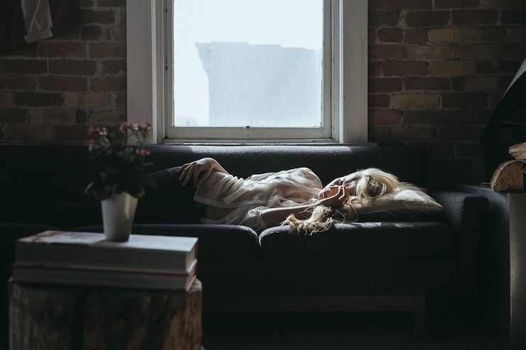 Tired woman laying on couch with hand on forehead