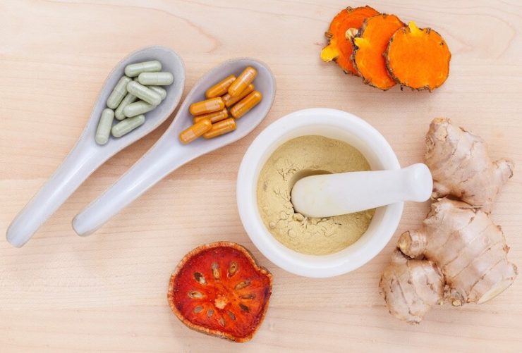 Mortar and pestle with powder and ceramic spoons with colorful capsules on a table