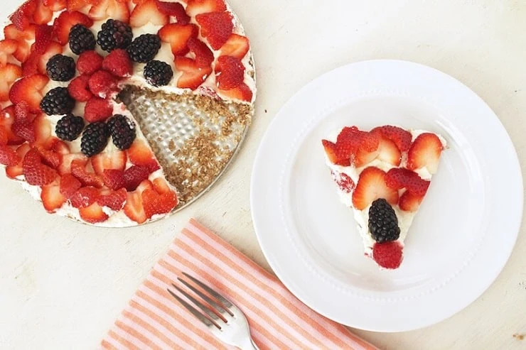A No Bake Fruit Tart on a plate with a slice cut out sitting on a white plate