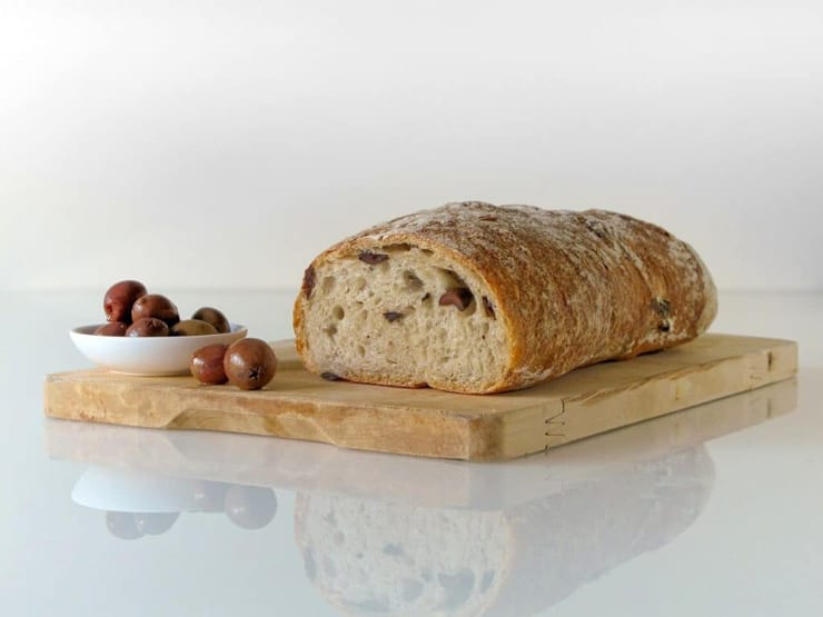 A loaf of ciabatta bread sitting on a wooden board with olives
