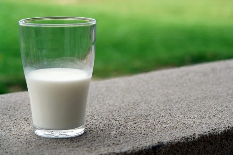 A half full glass of milk sitting on a wall outside