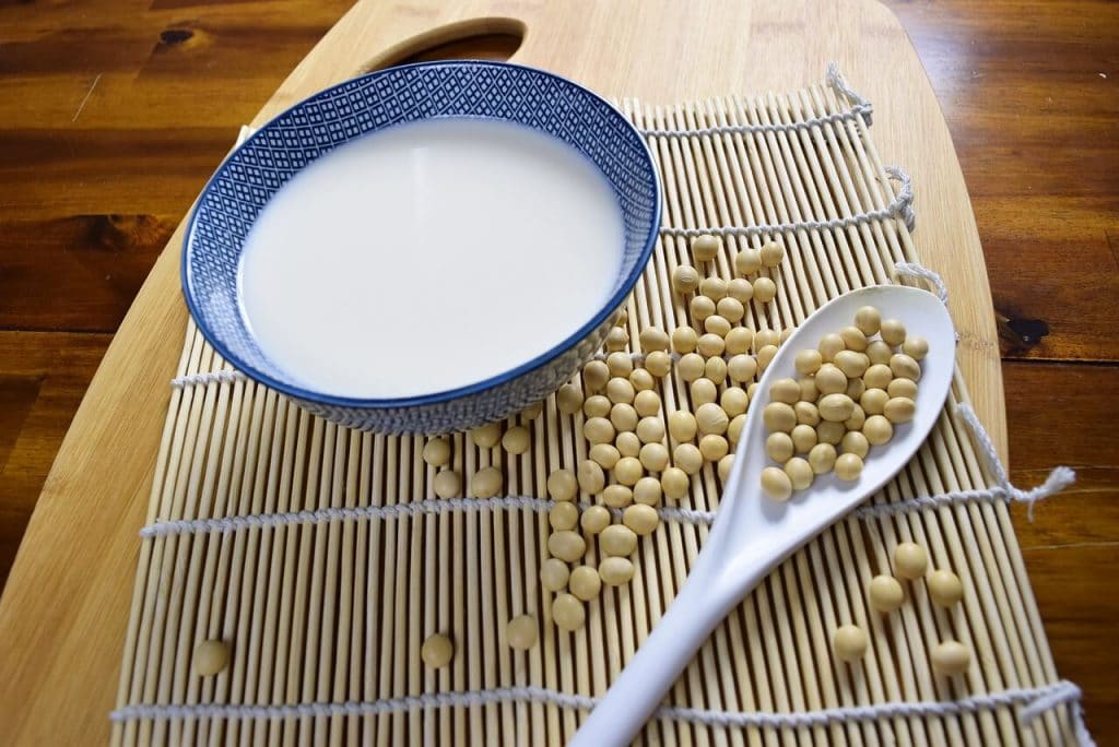 A bowl of milk sitting on a wooden table with soy beans at the side