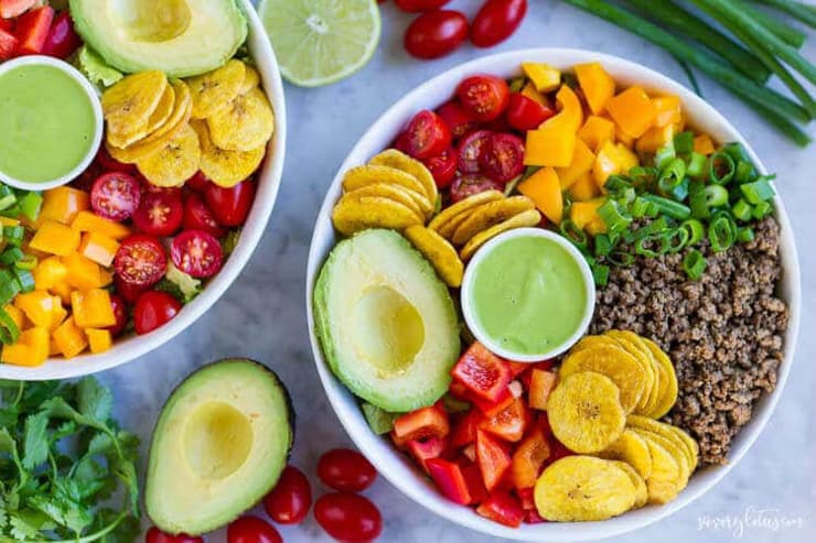 A bright and colorful taco salad bowl filled with fruit and veggies and green dipping sauce