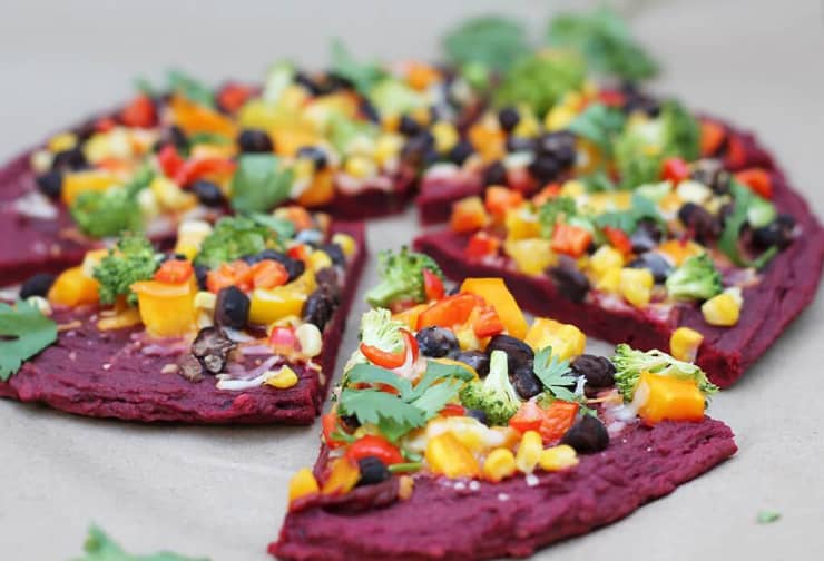 A healthy pizza crust made from beets sitting on a white surface with a slice cut out