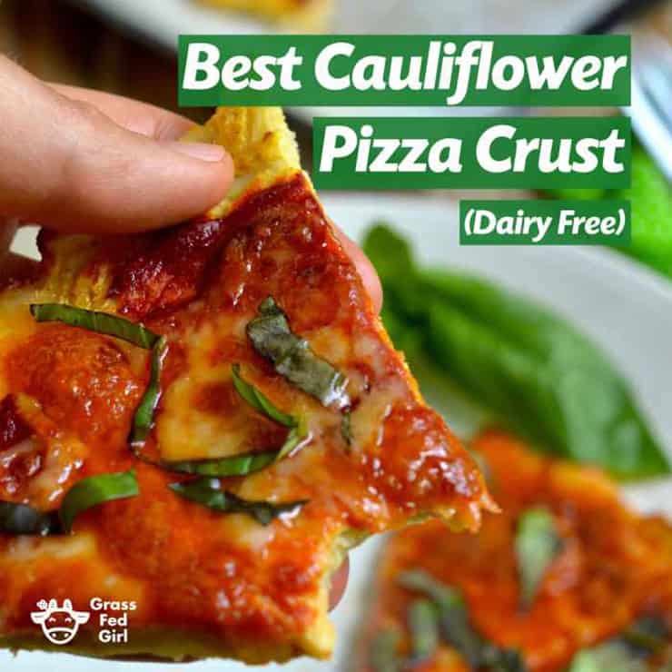 A hand holding a healthy pizza crust made from cauliflower with a tomato topping