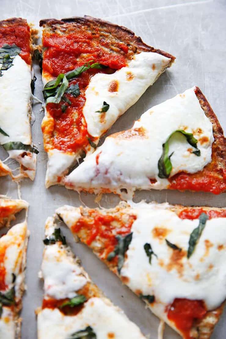 A close up of a healthy pizza crust cut into slices and topped with cheese and herbs