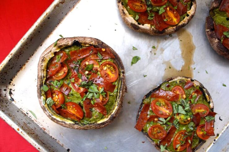 An overhead shot of healthy pizza portobello mushrooms on a baking tray topped with tomatoes and pesto