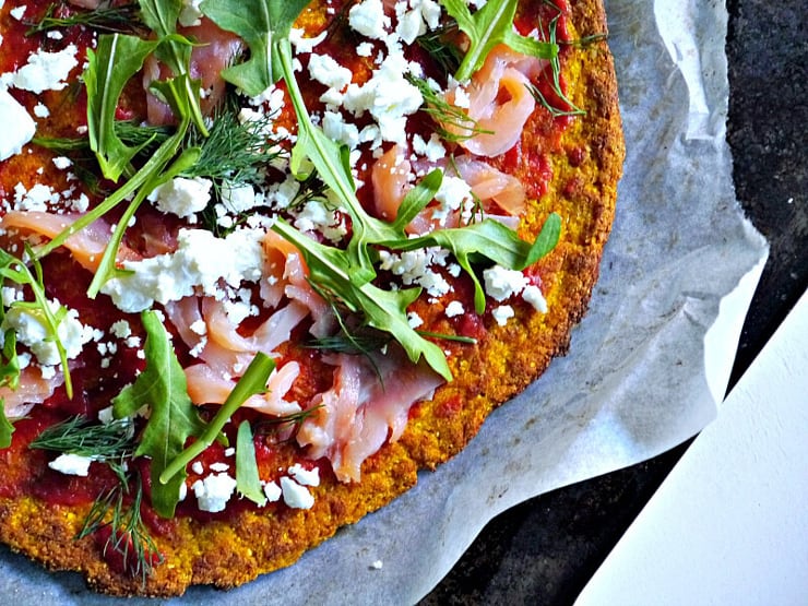 A close up of a healthy pizza crust with toppings sitting on top of baking parchment