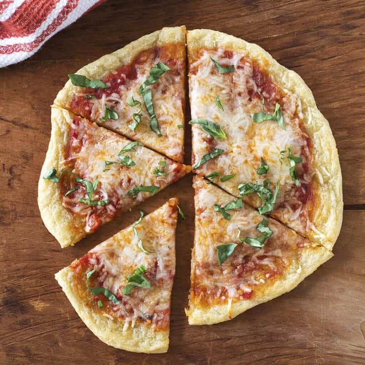 A round healthy pizza crust cut into slices sitting on a dark wooden board