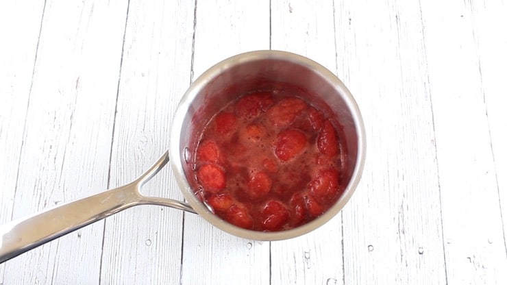 Cooked down strawberry in stainless steel pot on white wooden surface