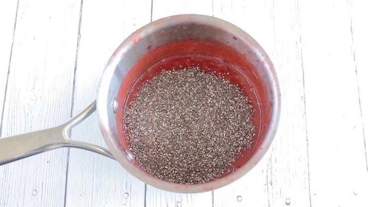 Cooked strawberry puree with chia seeds added on top in stainless steel pot on a white wooden surface