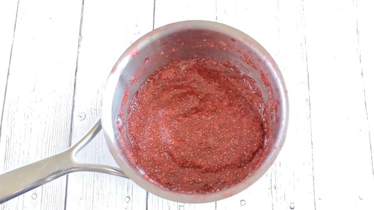 Finished chia strawberry jam in stainless steel pot on white wooden surface