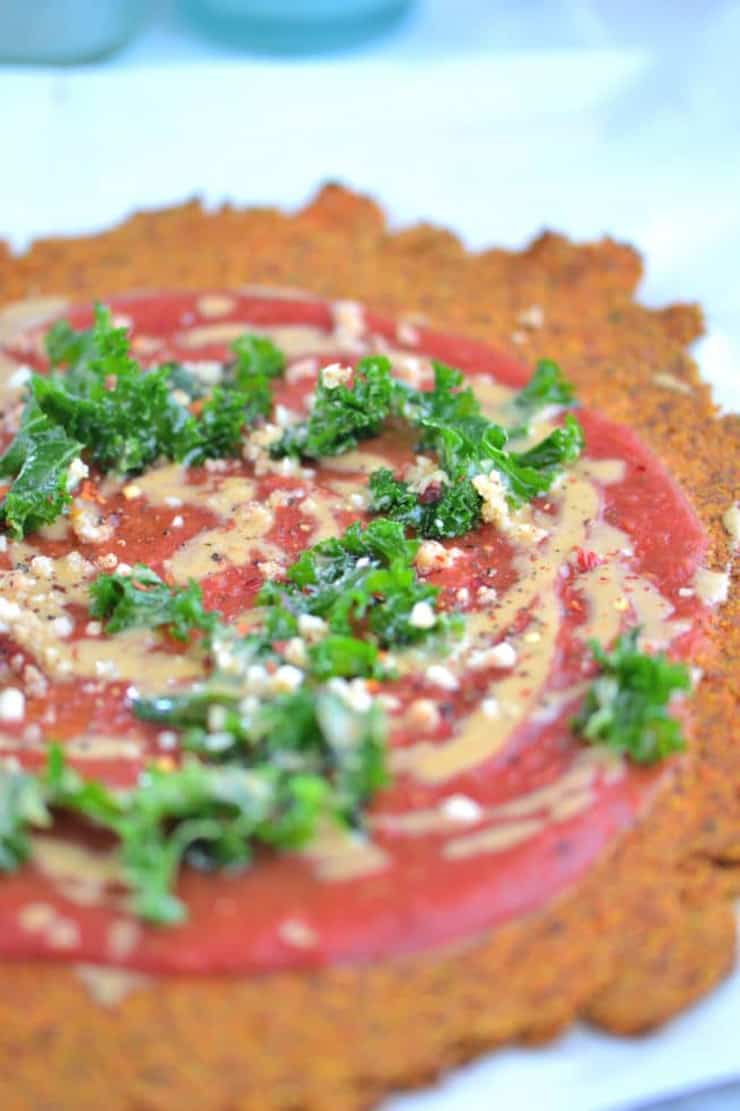 A close up of a healthy pizza crust on a white surface topped with tomato sauce and herbs