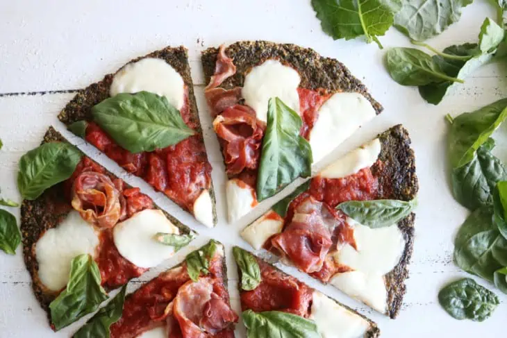 Overhead shot of green kael pizza crust topped with red tomato sauce and mozarella chunks