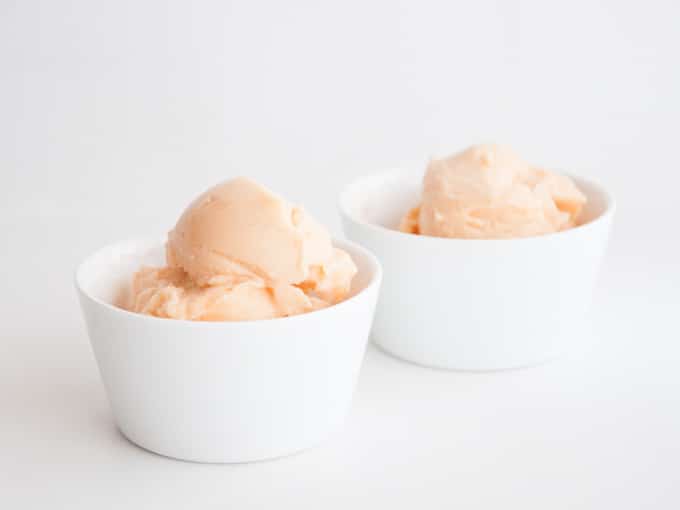 Two white cups of peach colored Cantaloupe Ice Cream with white background