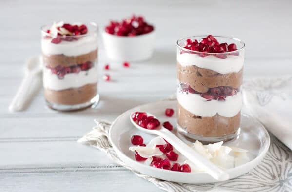 Layered chocolate, coconut pudding and pomegranate seeds in a clear glass on a white table