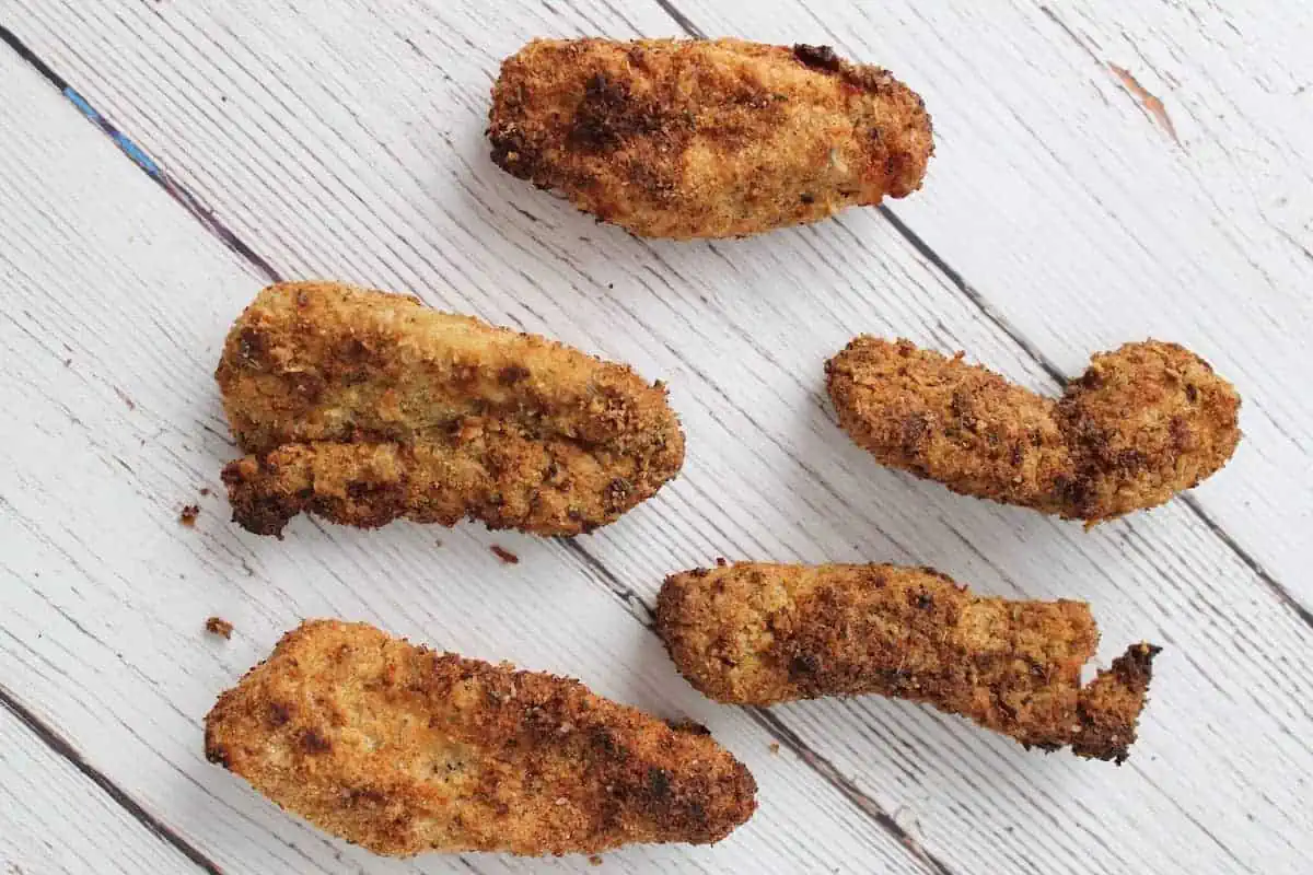 Close up of finished chicken fingers on a white wooden surface
